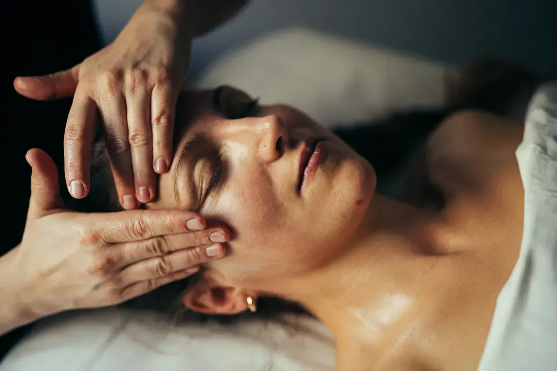 Manuel ansigtsmassage, mens klienten hviler med lukkede øjne.