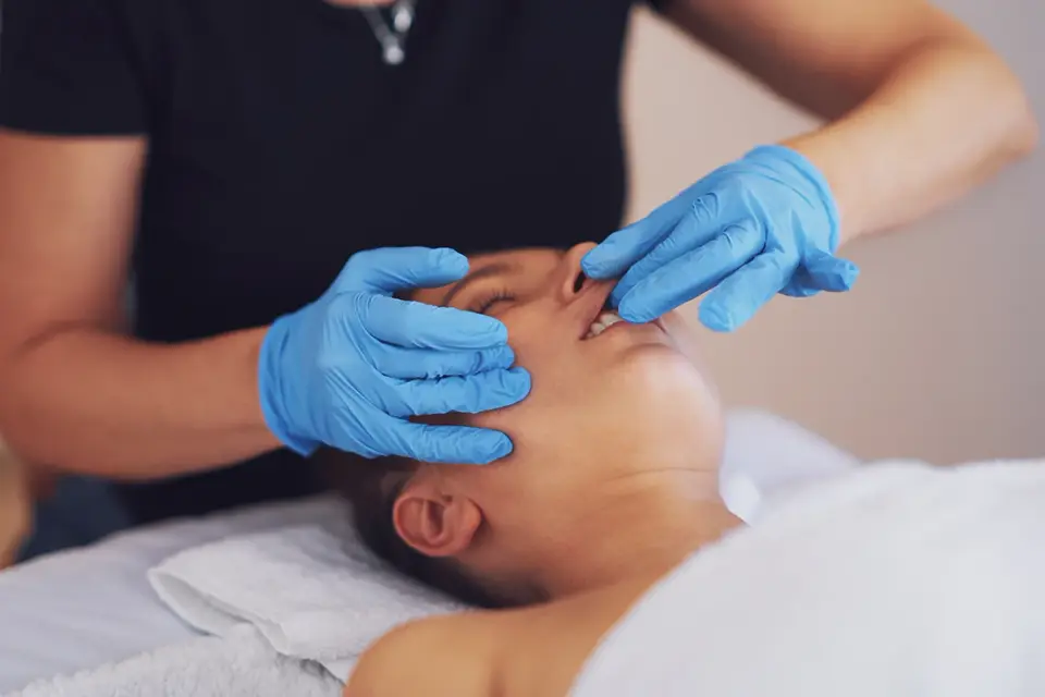 Nærbillede af hænder med handsker under intraoral kindmassage.