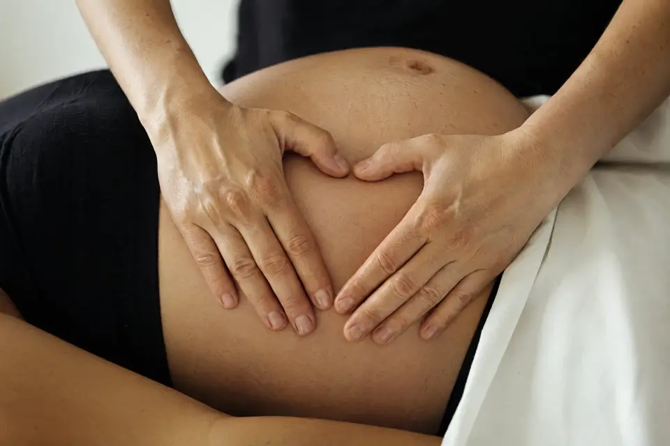 Hænder hvilende på en gravid mave – omsorg og ro under graviditeten.