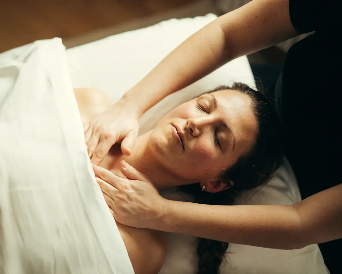 Blid massage omkring nakke og kraveben hos en liggende klient.