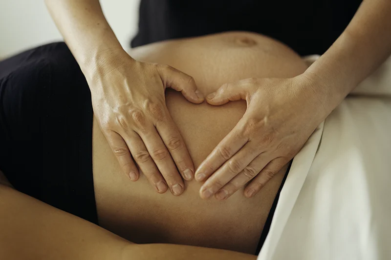 Hænderne på en massør, der udfører gravidmassage på en kommende mors mave